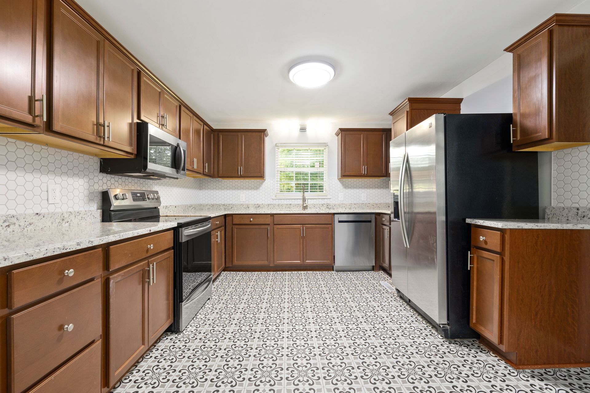 Spacious modern kitchen featuring wooden cabinets, unique tiled floor, and stainless steel appliances.